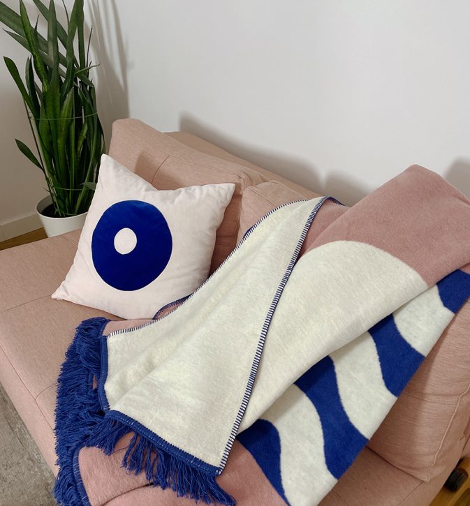 Designerski bawełniany koc Surfer Baltic Blue od Hogai. 150x200 cm – różowo granatowy wzór inspirowany Bałtykiem. Aranżacja z poduszką Hogai Dreamer