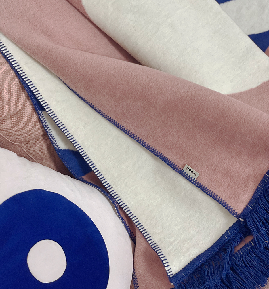 Designerski bawełniany koc Surfer Baltic Blue od Hogai. 150x200 cm – różowo granatowy wzór inspirowany Bałtykiem. Aranżacja z poduszką Hogai Dreamer