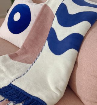 Designerski bawełniany koc Surfer Baltic Blue od Hogai. 150x200 cm – różowo granatowy wzór inspirowany Bałtykiem. Aranżacja z poduszką Hogai Dreamer