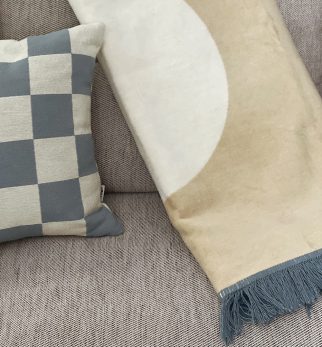 Designerski bawełniany koc Surfer Baltic Sand od Hogai. 15ox200 cm – beżowy surferski wzór inspirowany Bałtykiem. Aranżacja z poduszką Hogai Chess